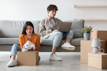 Young Couple on Moving Day With Girlfriend Unpacking While Boyfriend Plays Gamesの写真素材