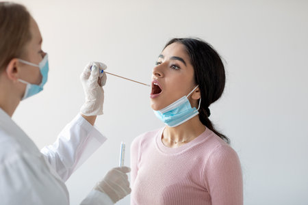 European Doctor Conducts Covid-19 Pcr Test on Young Indian Woman in Clinic Settingの写真素材