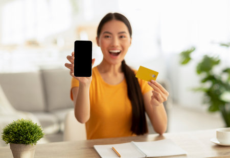 Overjoyed Woman Shows Blank Smartphone and Credit Card While Shopping Online From Homeの写真素材