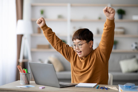 Chubby Asian Schooler Happily Celebrates Academic Success at Home With Notebook and Laptopの写真素材