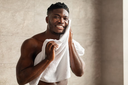 Cheerful African American Male Enjoying Skincare After Washing Face in Modern Bathroomの写真素材