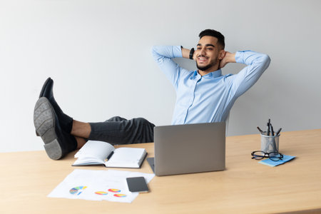 Young Arab Man Enjoying a Relaxing Break at His Workspace While Using a Laptopの写真素材