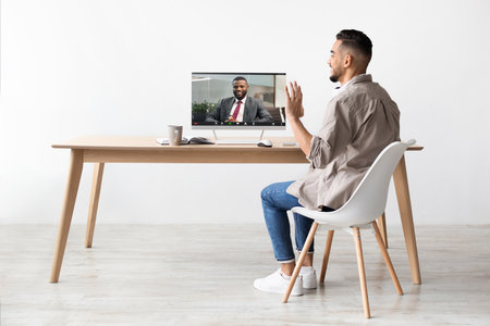 Young Arab Man Engages in Video Call With Colleague From His Office, Smiling and Wavingの写真素材