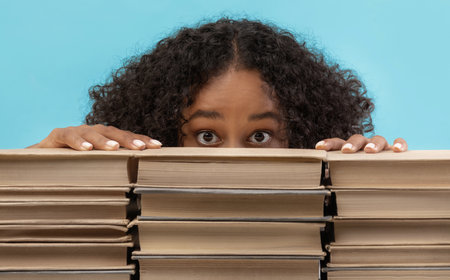 Scared Female Student Hiding Behind Books in Preparation for College Exams in a Blue Studioの写真素材