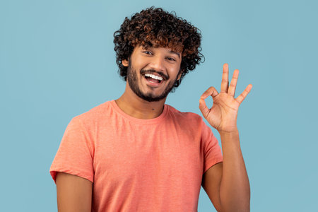 Happy Young Eastern Man Showing Okay Gesture on Blue Background in Studio Settingの写真素材