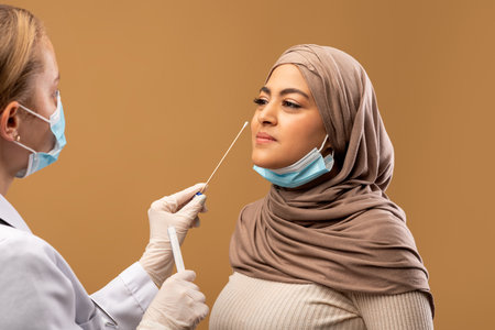 COVID-19 pcr test concept. Medical worker taking nasal swab for coronavirus sample test from infected muslim womanの写真素材