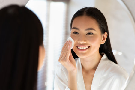Mirror Reflection of Young Asian Woman Caring for Her Skin With Cotton Padの写真素材