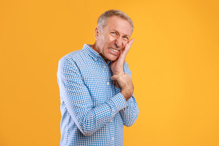 Unhappy Man Touching His Cheek Due to Severe Toothache on Bright Yellow Backgroundの写真素材