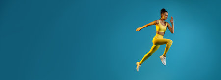 Athletic Female in Mid-Air Running Pose Against Blue Background for Sport Motivationの写真素材
