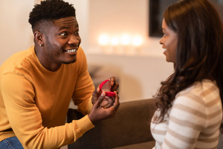 Excited Black Man Proposes With Engagement Ring at Home on Cozy Couch
