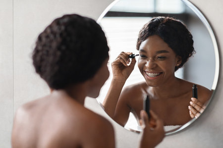 Beautiful Young Lady Smiles While Applying Mascara in Bathroom Mirrorの写真素材