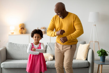 Grandfather and Granddaughter Joyfully Dance Together in Cozy Living Roomの写真素材