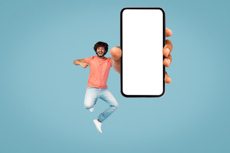 Happy Young Man Jumping With Smartphone Against Blue Background for Mockup