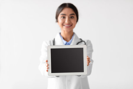 Smiling Millennial Woman Doctor Displays Empty Digital Tablet in Medical Uniformの写真素材