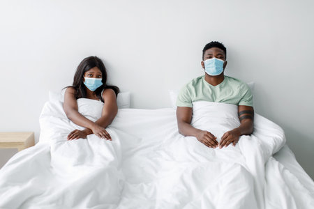 Couple Wearing Face Masks Sitting in Bed Looking Apart During Pandemicの写真素材