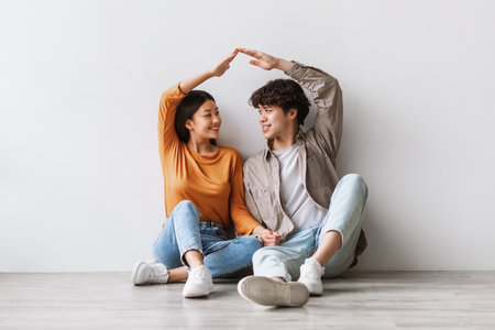 Joyful Asian Couple Celebrating New Home by Creating a Roof With Their Handsの写真素材
