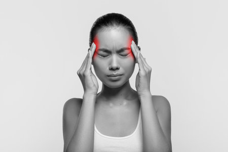 Young Woman Experiencing Severe Headache While Rubbing Her Temples in Studio Settingの写真素材