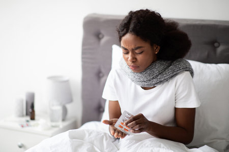African American Lady Sitting in Bed Taking Medication While Feeling Unwell at Homeの写真素材