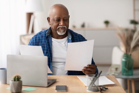 Mature Black Businessman Reviews Bills and Documents at Modern Office Deskの写真素材