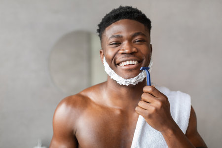 Happy African American Man Shaving in Modern Bathroom Smiling at Cameraの写真素材