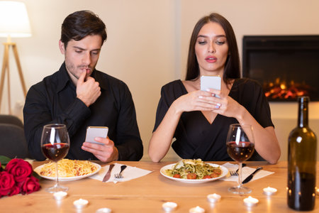 Couple Dining at a Table With Pasta and Red Wine While Distracted by Their Phones in a Cozy Roomの写真素材