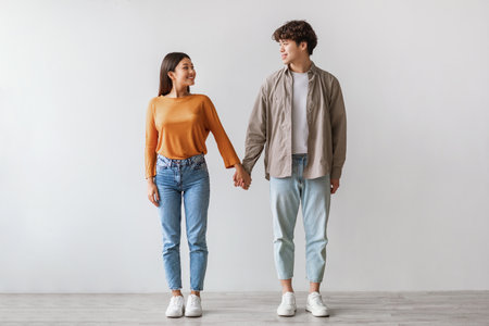 Millennial Couple in Love Smiling While Standing Together Against a White Studio Wallの写真素材
