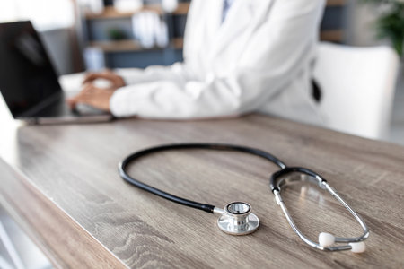 Doctor Using Laptop at Clinic Desk With Stethoscope in Focus, Highlighting Healthcare Activityの写真素材