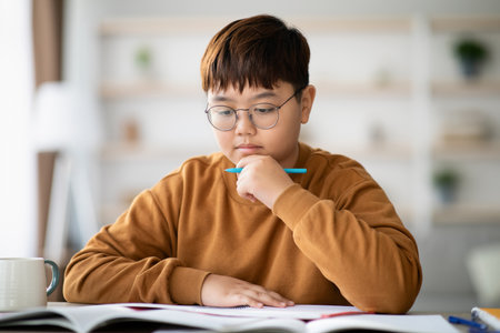 Smart Korean Teen Boy Studying at Home While Doing Homework Tasks With Focus and Determinationの写真素材