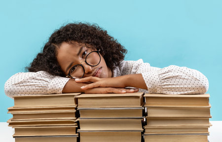 Young Female Student Feeling Bored While Studying for Exams With Stacks of Books Around Herの写真素材