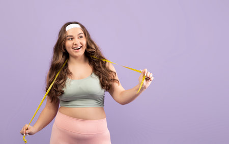 Plus Size Young Woman Surprised With Measuring Tape in Sportswear Against Violet Background
