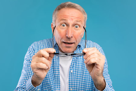 Mature Man in Blue Studio Shocked While Taking off Glasses and Staring at the Camera