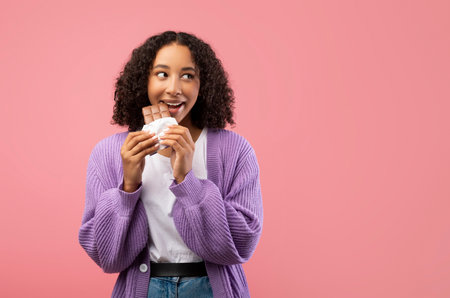Cheerful African American Lady Enjoys Chocolate Treat Against Pink Background in Studio