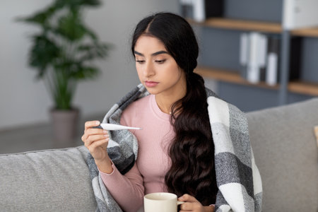 Young Hindu Woman Feeling Unwell With High Fever at Home While Holding a Hot Drink