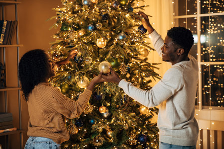 Young Black Couple Joyfully Decorating Their Christmas Tree at Home for the Holiday Seasonの写真素材