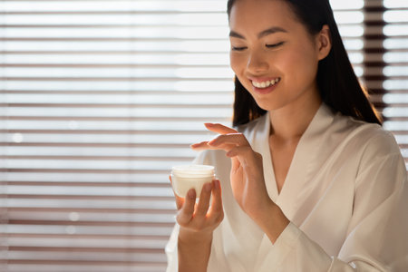 Smiling Chinese Woman Enjoys Her Morning Skincare Routine by the Windowの写真素材