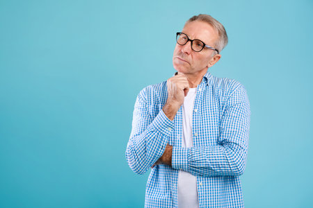 Mature Man in Glasses Contemplating Life Decisions in Blue Studio Backgroundの写真素材