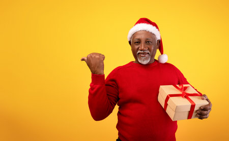 Happy Senior Man in a Red Sweater and Santa Hat Holds a Gift for a Holiday Announcementの写真素材