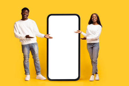 Happy Young Couple Showcases a Blank Smartphone on a Bright Yellow Background