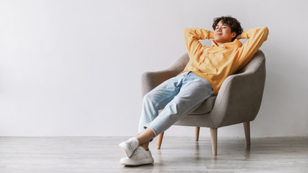Young Asian Man Enjoys a Lazy Break in a Cozy Armchair Against a Clean White Wallの写真素材
