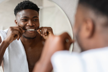 Cheerful Man Caring for Teeth and Smiling in Modern Bathroom While Flossingの写真素材