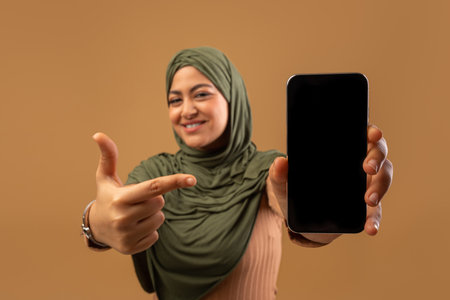 Happy Arab Woman Showcasing Smartphone for App Mockup Against a Neutral Backgroundの写真素材