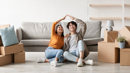 Cheery Millennial Couple Celebrates New Home With House Roof Gesture on Moving Dayの写真素材