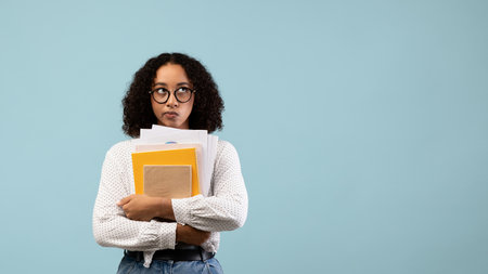 Thoughtful African American Student With Notebooks in a Blue Studio Settingの写真素材