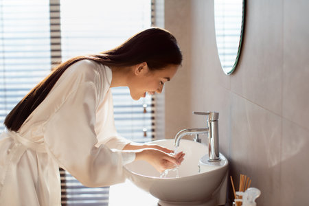Young Japanese Lady Washing Her Face in a Beautiful Bathroom During the Morningの写真素材