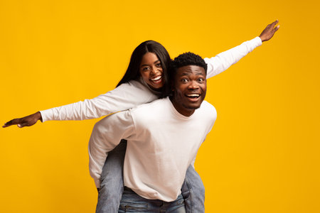 Joyful Couple Having Fun in Playful Pose Against Bright Yellow Backgroundの写真素材