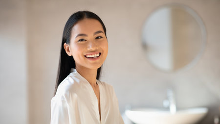 Cheerful Chinese Lady Smiling in a Bright Bathroom During Her Beauty Routineの写真素材