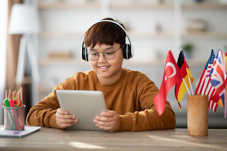 Chubby Asian Boy With Glasses Learns Foreign Language Using Tablet and Headset at Homeの写真素材