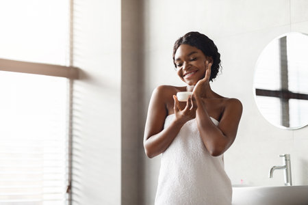 Sensual Black Lady Enjoying Her Beauty Routine in a Modern Bathroom After a Refreshing Showerの写真素材