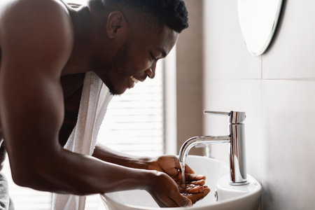 African American Guy Performing Morning Self-Care Routine in a Modern Bathroom With Wash-Basinの写真素材