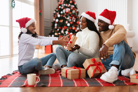 Happy Black Family Celebrates Christmas Exchanging Gifts in Cozy Living Roomの写真素材